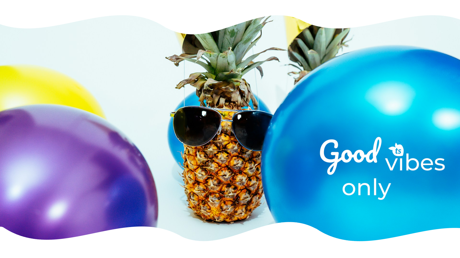 Pineapple wearing sunglasses with colorful balloons and 'Good vibes only' text on a white background