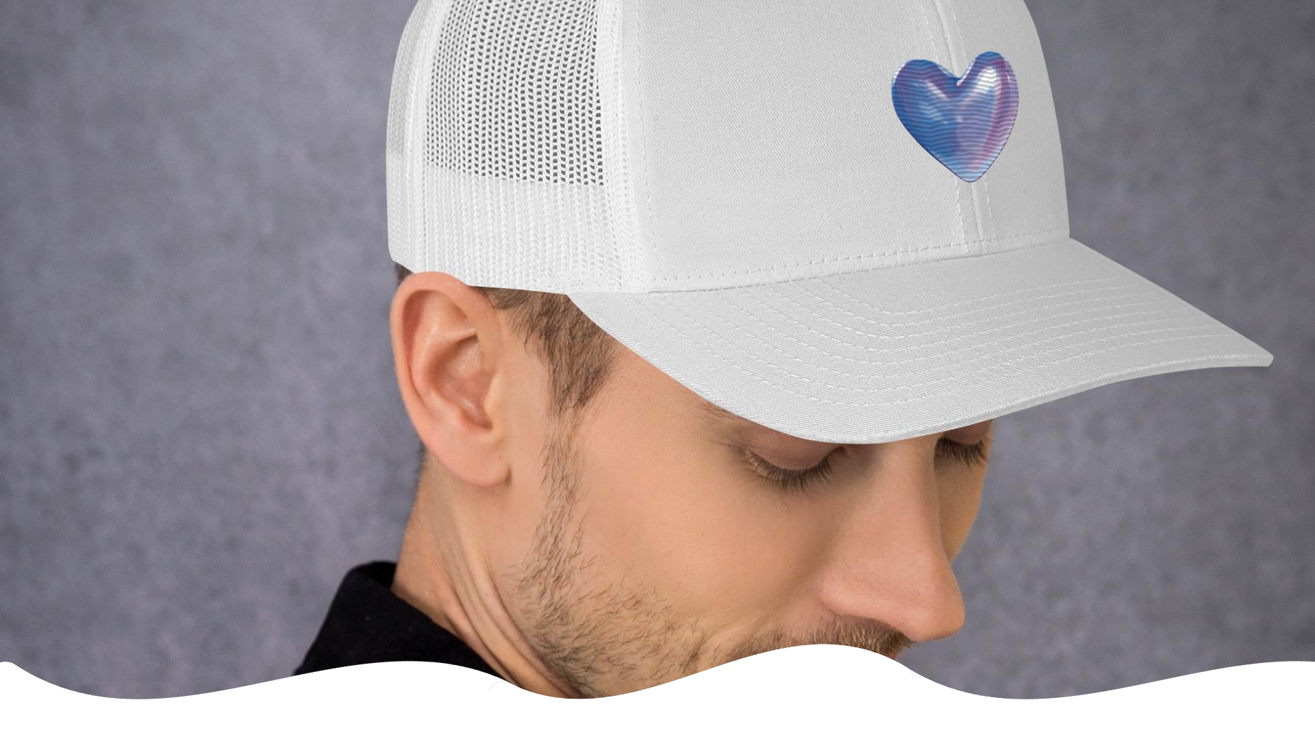 White cap with a colorful heart design worn by a person against a gray background