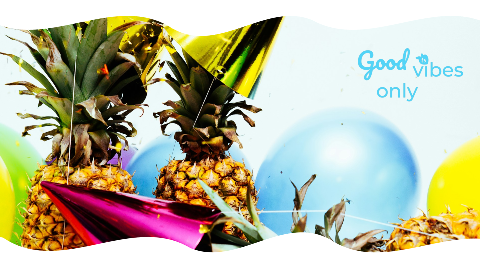 Two pineapples with colorful party hats on a beach with 'Good Vibes only' text.